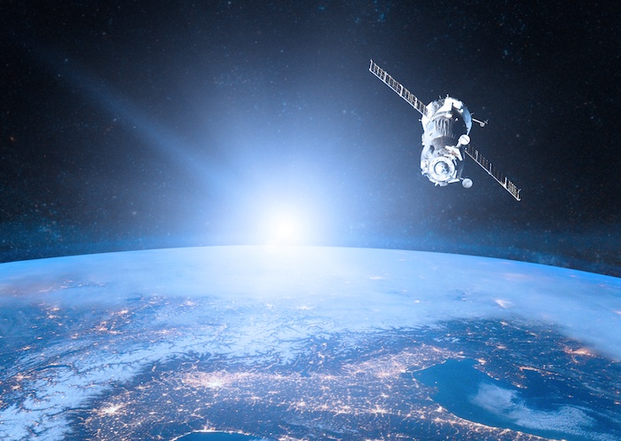 Satellite above earth with sun on the horizon